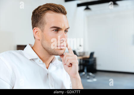 Primo piano della pensieroso giovane imprenditore seduto e pensare in ufficio Foto Stock