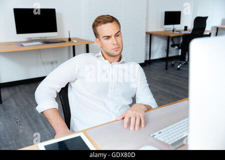 Grave giovane impreditore seduti al posto di lavoro e utilizzando il computer in ufficio Foto Stock