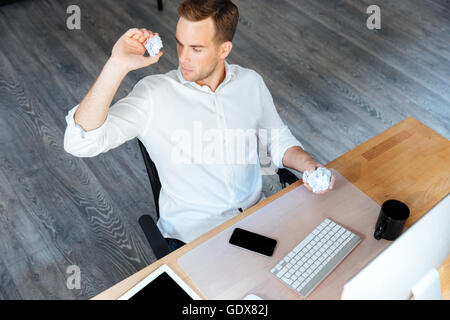 Vista superiore della grave giovane imprenditore di gettare la carta stropicciata e lavoro in ufficio Foto Stock