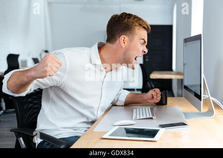 Furious aggressiva giovane impreditore gridando e lavorare con il computer in ufficio Foto Stock