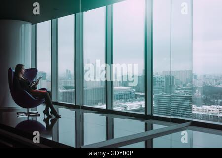 Silhouette di giovane donna di affari con la compressa seduto su una sedia, in inverno il paesaggio della città Foto Stock