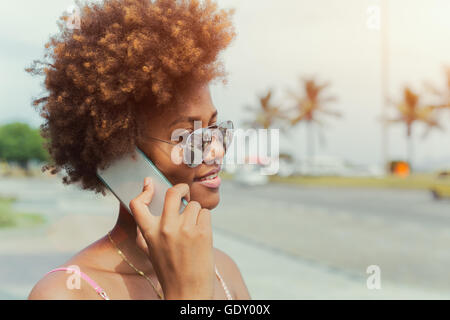 Felice americano africano giovane donna in occhiali da sole chiamando sullo smartphone Foto Stock
