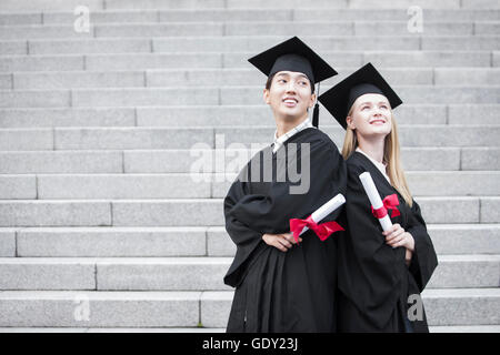 Maschio sorridente college graduate e sorridente collegio femminile laureato di schiena con le braccia conserte cercando Foto Stock