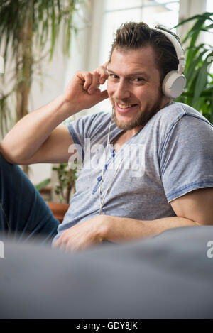 Metà uomo adulto ascoltando musica in soggiorno, Monaco di Baviera e sorridente, Baviera, Germania Foto Stock