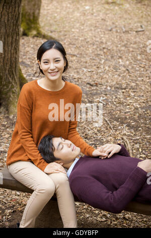 Giovane coppia romantica avente una data sul banco nel bosco in autunno Foto Stock