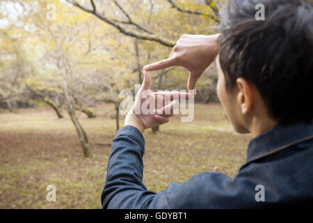 Indietro Ritratto di giovane uomo che fa un dito telaio contro gli alberi di autunno Foto Stock