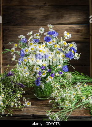 Bouquet di chamomiles e cornflowers nel vaso sul tavolo di legno. Foto Stock