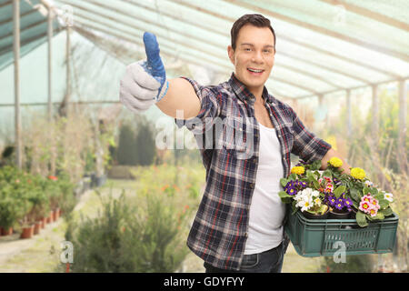 Giovane ragazzo dando un pollice in alto e tenendo un cesto di fiori in una serra Foto Stock