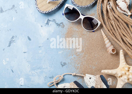 Accessori da spiaggia. Occhiali da sole, flip-flop e conchiglie di mare su sfondo di pietra. Vista da sopra con lo spazio di copia Foto Stock