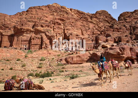 Un uomo beduino in sella al suo cammello con le tombe reali in background, Petra, Giordania Foto Stock