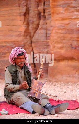 Un musicista beduino suonando e cantando nella parte esterna Siq di Petra, Giordania Foto Stock