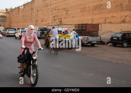 Street View di Marrakech, con una donna musulmana alla guida di una moto con una rosa hijab Foto Stock