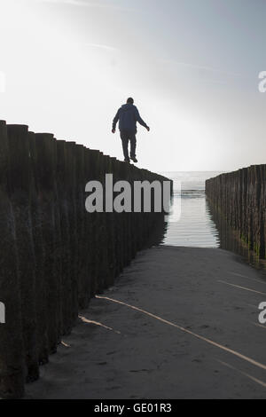 Silhouette di un uomo maturo in equilibrio su palo di legno sulla spiaggia, Renesse, Schouwen-Duiveland, Zeeland, Paesi Bassi Foto Stock