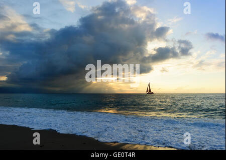 Barca a vela silhouette raggi di sole è un burst raggi di sole con la ripresa attraverso le nuvole come una barca a vela si sposta lungo l'acqua verso t Foto Stock