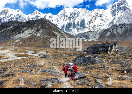 Facchini con carico pesante dopo aver attraversato Cho La Pass in Himalaya, situato a 5,420 metri (17,782 ft) sopra il livello del mare in Solukhumbu. Foto Stock