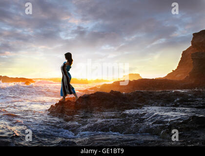 Donna in piedi su rocce dall'oceano al tramonto, Orange County, California, Stati Uniti Foto Stock