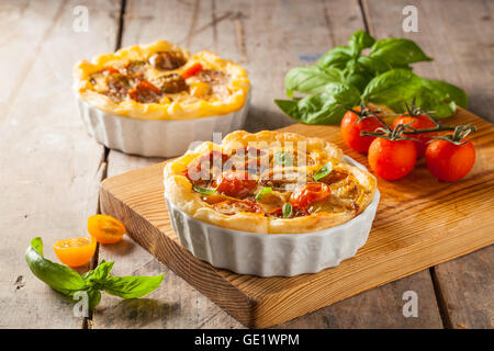 Quiche con pomodori ciliegia su una tavola in legno rustico. Foto Stock