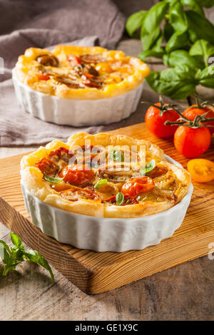 Quiche con pomodori ciliegia su una tavola in legno rustico. Foto Stock