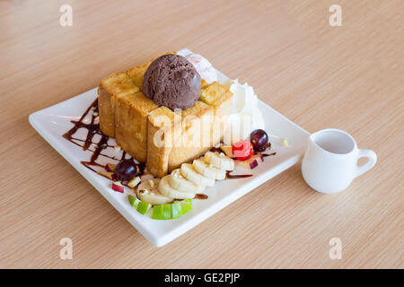 Toast al miele e panna montata con gelato al cioccolato su uno sfondo di legno Foto Stock