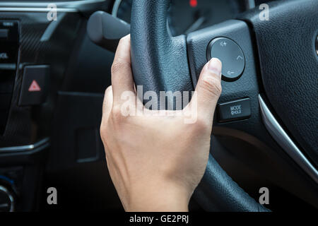 Una donna mano spinge il pulsante di controllo del volume su un volante. Foto Stock