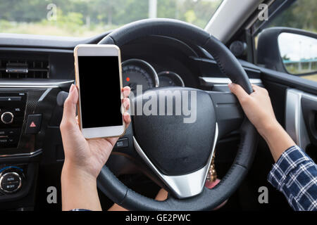 Femmina giovane conducente utilizzando il touch screen smartphone e mano che tiene il volante in un'auto. Foto Stock