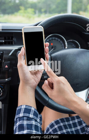 Femmina giovane conducente utilizzando il touch screen smartphone in un'auto. Foto Stock