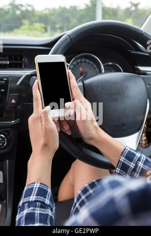 Femmina giovane conducente utilizzando il touch screen smartphone in un'auto. Foto Stock