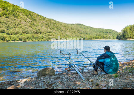 Le avventure di pesca, la pesca alla carpa. Pescatore sulle rive di un lago Foto Stock