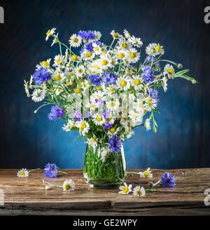 Bouquet di chamomiles e cornflowers nel vaso sul tavolo di legno. Foto Stock