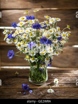 Bouquet di chamomiles e cornflowers nel vaso sul tavolo di legno. Foto Stock