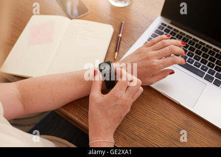 Close up smartwatch sulla donna la mano, ella è utilizzando la smart orologio da polso mentre è seduto alla sua scrivania. Foto Stock