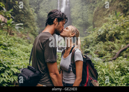 Colpo di amorevole coppia giovane kissing permanente, mentre nella foresta. Matura in amore kissing nei pressi di una cascata nella foresta. Foto Stock