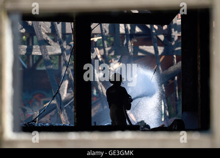 Berlin-Britz, Germania. 22 Luglio, 2016. Un incendio fighter durante la fase finale delle opere di estinzione sui terreni della ex pubblico leisure pool "blub" in Berlin-Britz, Germania, 22 luglio 2016. Fino a 100 vigili del fuoco con sei camion erano occupate estinguere il fuoco durante la notte. L'ex pubblica popolare piscina per il tempo libero "blub" è stato chiuso nel 2005. L'edificio è detto di essere abbattuto. 450 nuovi appartamenti sono pianificate per essere costruito sui terreni la misura 35.000 metri quadrati. Foto: RAINER JENSEN/dpa/Alamy Live News Foto Stock