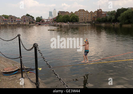 Shadwell, Londra. Regno Unito. Il 23 luglio 2016. Per coloro che godono di slacklining durante le calde giornate di sole a Shadwell bacino nella zona est di Londra questo pomeriggio. Slacklining è lo sport di bilanciamento su una striscia di nastro che è fisso in alto sopra il terreno ma non stirato in modo da essere teso. Le persone sono stati avvertiti di non nuotare nel bacino Shadwell dopo un uomo annegato e morto questa settimana. Credito: Vickie Flores/Alamy Live News Foto Stock