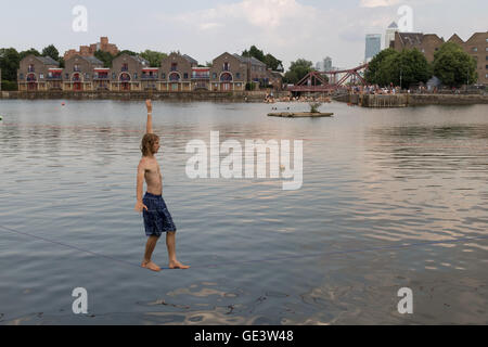 Shadwell, Londra. Regno Unito. Il 23 luglio 2016. Per coloro che godono di slacklining durante le calde giornate di sole a Shadwell bacino nella zona est di Londra questo pomeriggio. Slacklining è lo sport di bilanciamento su una striscia di nastro che è fisso in alto sopra il terreno ma non stirato in modo da essere teso. Le persone sono stati avvertiti di non nuotare nel bacino Shadwell dopo un uomo annegato e morto questa settimana. Credito: Vickie Flores/Alamy Live News Foto Stock