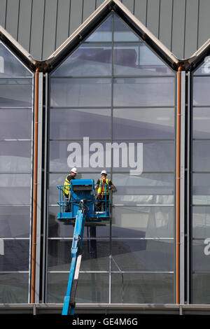 I lavori di costruzione nel Regno Unito: due lavoratori in una posizione elevata 'cherry picker' di lavoro della piattaforma sulla parte esterna di vetri di una nuova Tesco un Marks & Spencer retail outlet, Aberystwyth Wales UK Foto Stock