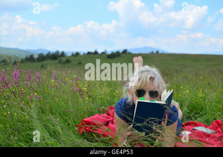 Donna relax su una coperta di rosso in un prato di montagna e la lettura di un libro Foto Stock