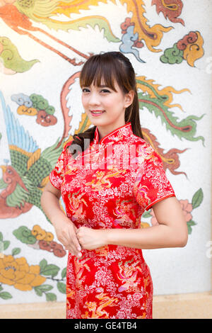 Felice anno nuovo cinese. Carino donna asiatica con gesto di congratulazione isolato sul rosso modello cinese sfondo tradizionale Foto Stock