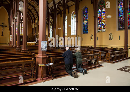 Una coppia di anziani prega all'interno di una chiesa cattolica cristiana presso la città di Cork in Irlanda meridionale Foto Stock