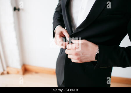 Rendere l'azienda guardare bene. Close-up di uomo abbottonatura suo giubbetto mentre in piedi contro lo sfondo grigio Foto Stock
