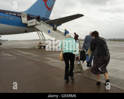 Linee aeree economiche. Passeggeri combattendo contro il vento e la pioggia per attraversare la pista di atterraggio per raggiungere il loro volo, Thompson Airways Boeing 757-204 aeromobili vincolati per Tenerife Foto Stock