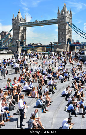 Caldo giorno di Londra affollato lavoratori di uffici e turisti all'aperto durante la pausa pranzo estiva intorno all'anfiteatro Scoop Tower Bridge River Tamigi Inghilterra Regno Unito Foto Stock