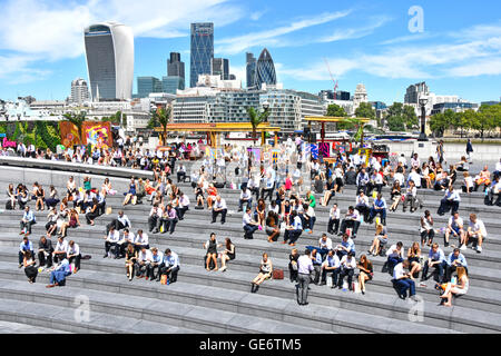 Ufficio di Southwark lavoratori tenuto caldo del soleggiato pausa pranzo al più Londra Scoop riverside anfiteatro con City Of London skyline al di là dell'Inghilterra, Regno Unito Foto Stock