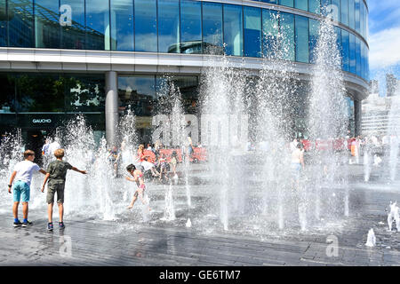 Getti di acqua che si eleva al di sopra del blocco di pavimentazione temporizzazioni casuale durante il caldo Londra UK estate meteo come ufficio di assumere lavoratori in pausa pranzo & bambini giocare in fontane Foto Stock