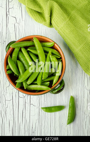 Una tazza di zucchero fresche snap di piselli e un asciugamano da cucina su un bianco tavolo di legno. Foto Stock