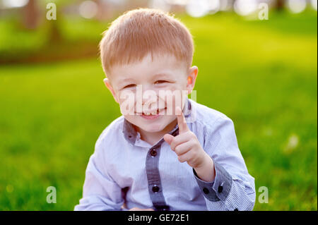 Allegro piccolo ragazzo seduto sull'erba nel parco Foto Stock