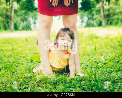 Un anno di vecchia bambina tra madre gambe all'aperto Foto Stock