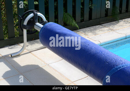 Copertura per piscina sul suo rullo all'estremità della piscina Foto Stock