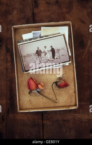 Vecchia scatola contenente la risma di vintage in bianco e nero alle foto di famiglia e due rossi secchi rosebuds Foto Stock