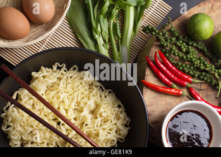 Tagliatelle in nero ciotola guarnendo il piatto sul tavolo da cucina Foto Stock